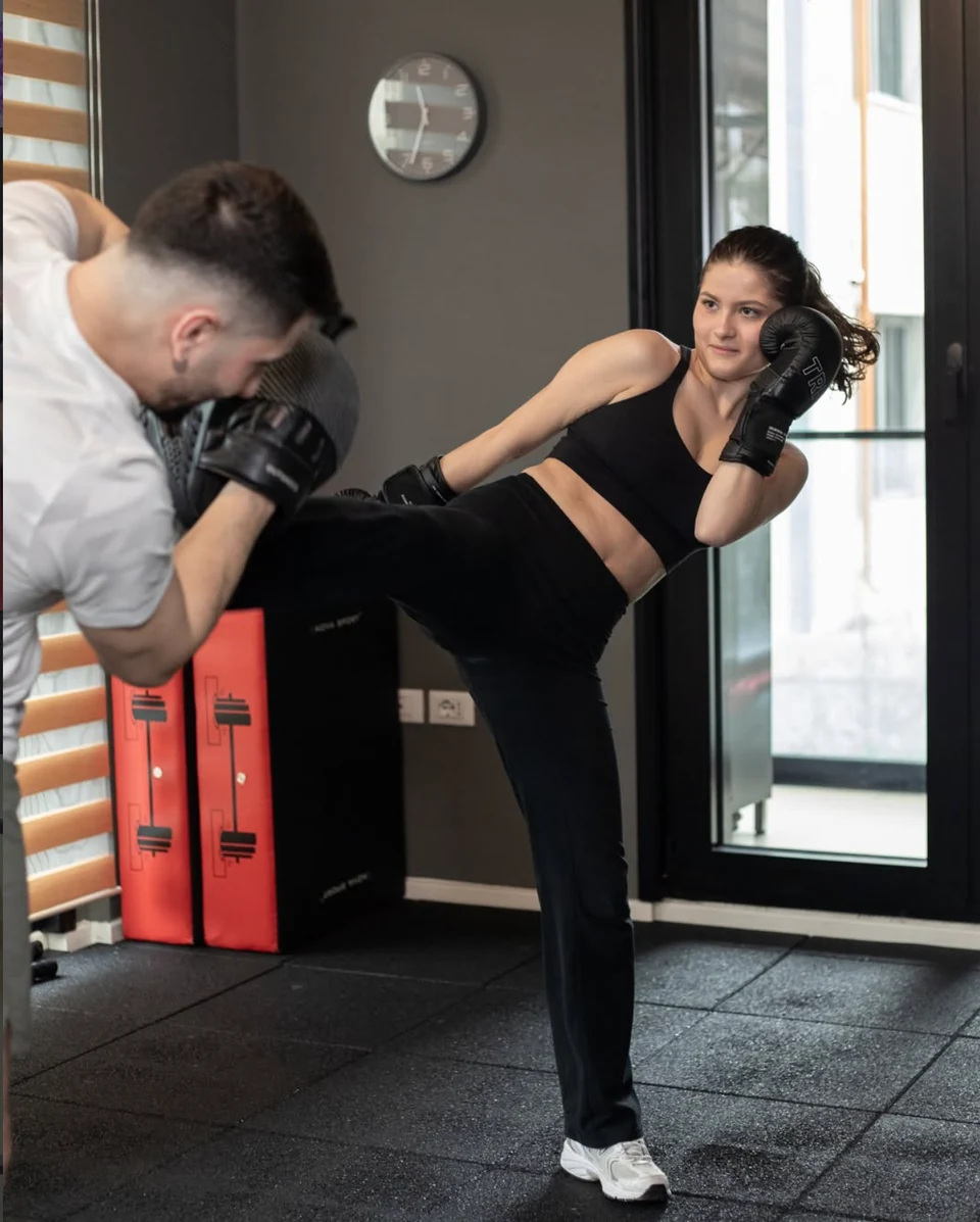 Një pjesëmarrëse duke ushtruar kickboxing me instruktorin në studio